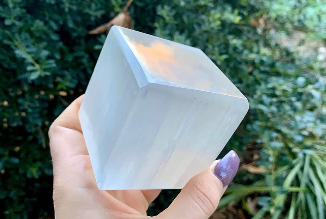 A hand holding a selenite crystal point outdoors