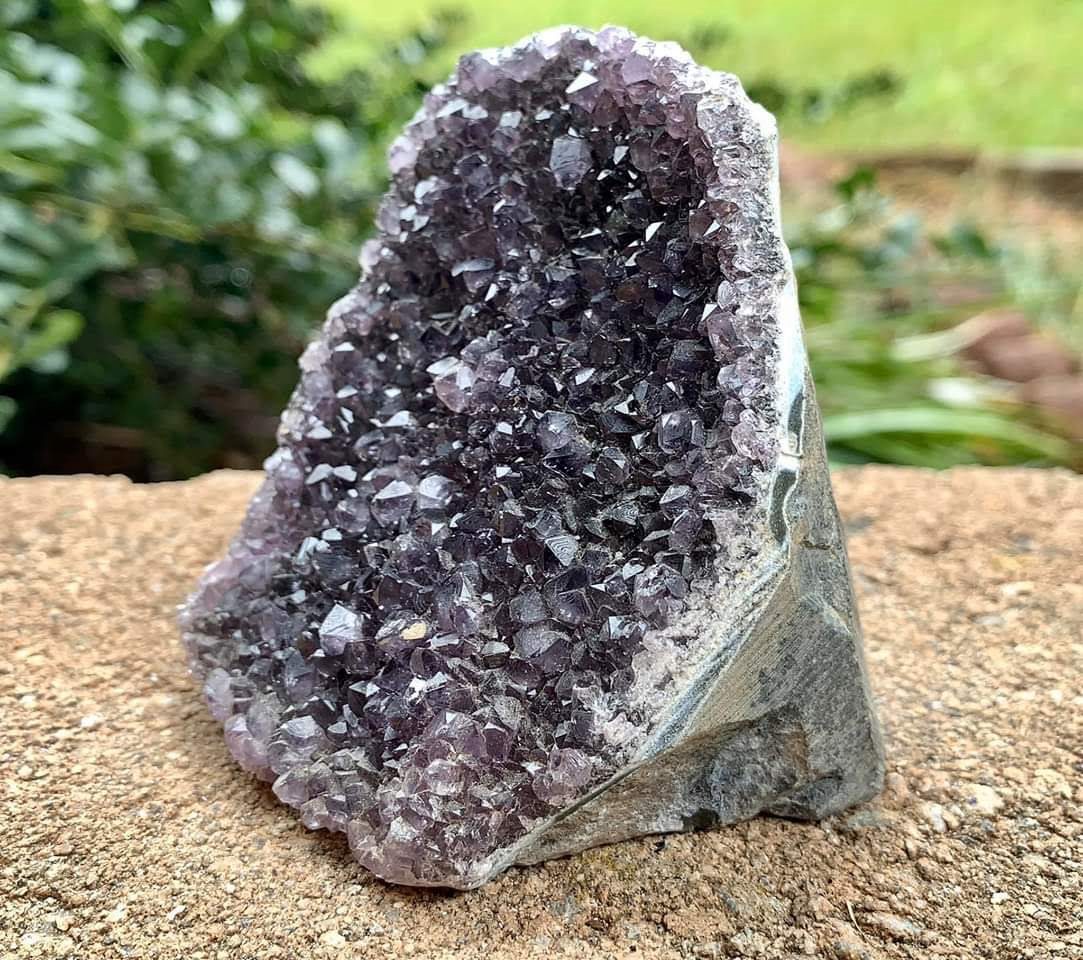 A raw amethyst geode cluster resting on stone