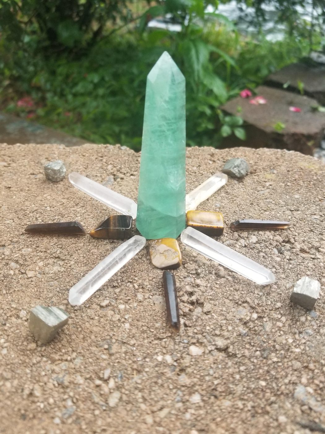A real crystal grid arranged outdoors with a green fluorite tower, clear quartz points, tiger's eye, and pyrite